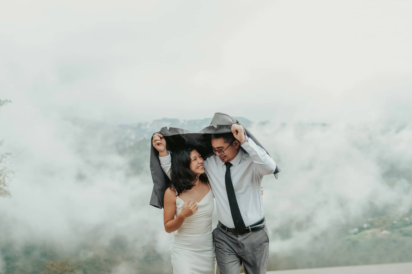The couple laughing together under his jacket, high up in the clouds