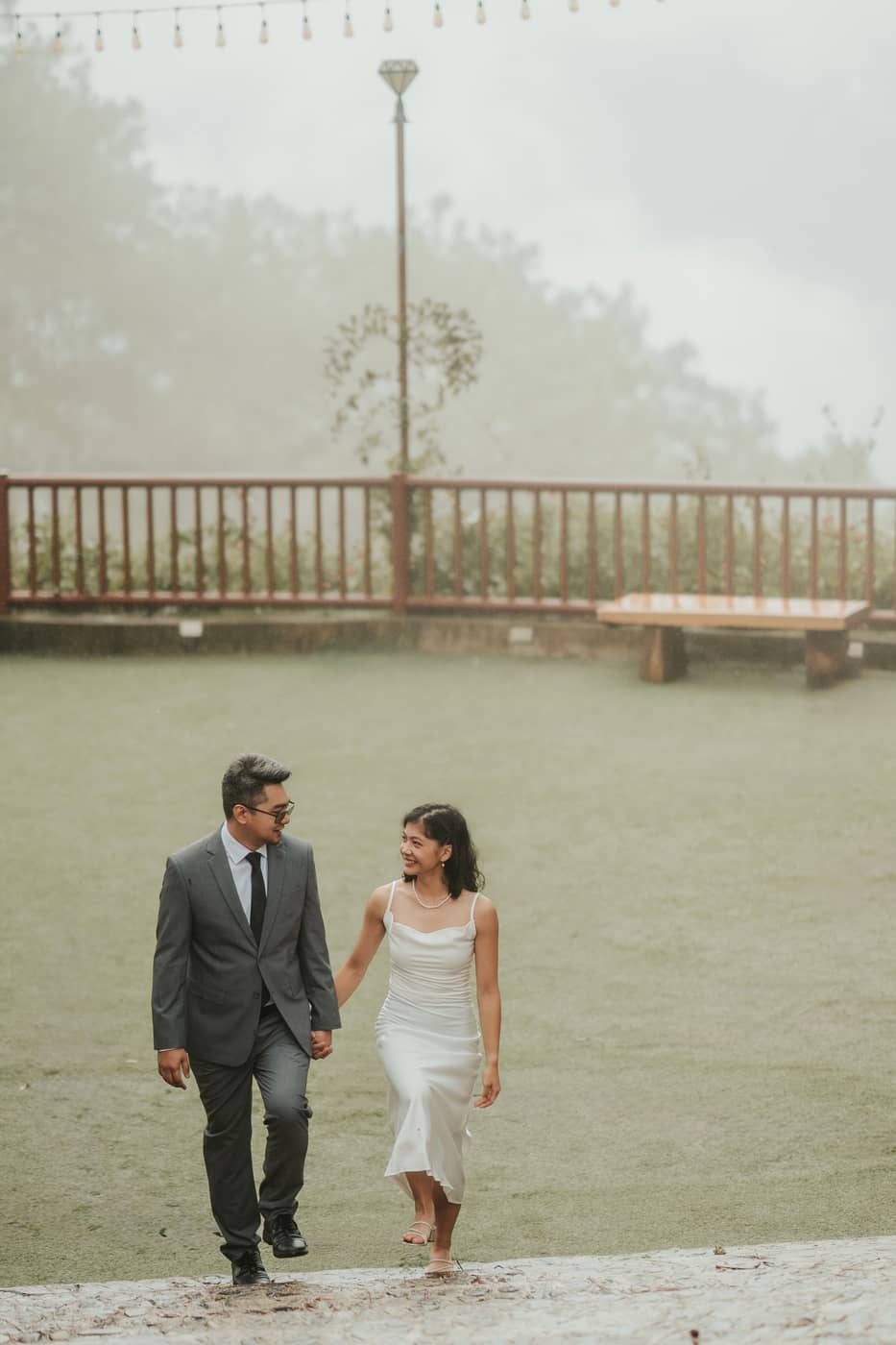 The couple walking hand in hand across a misty lawn