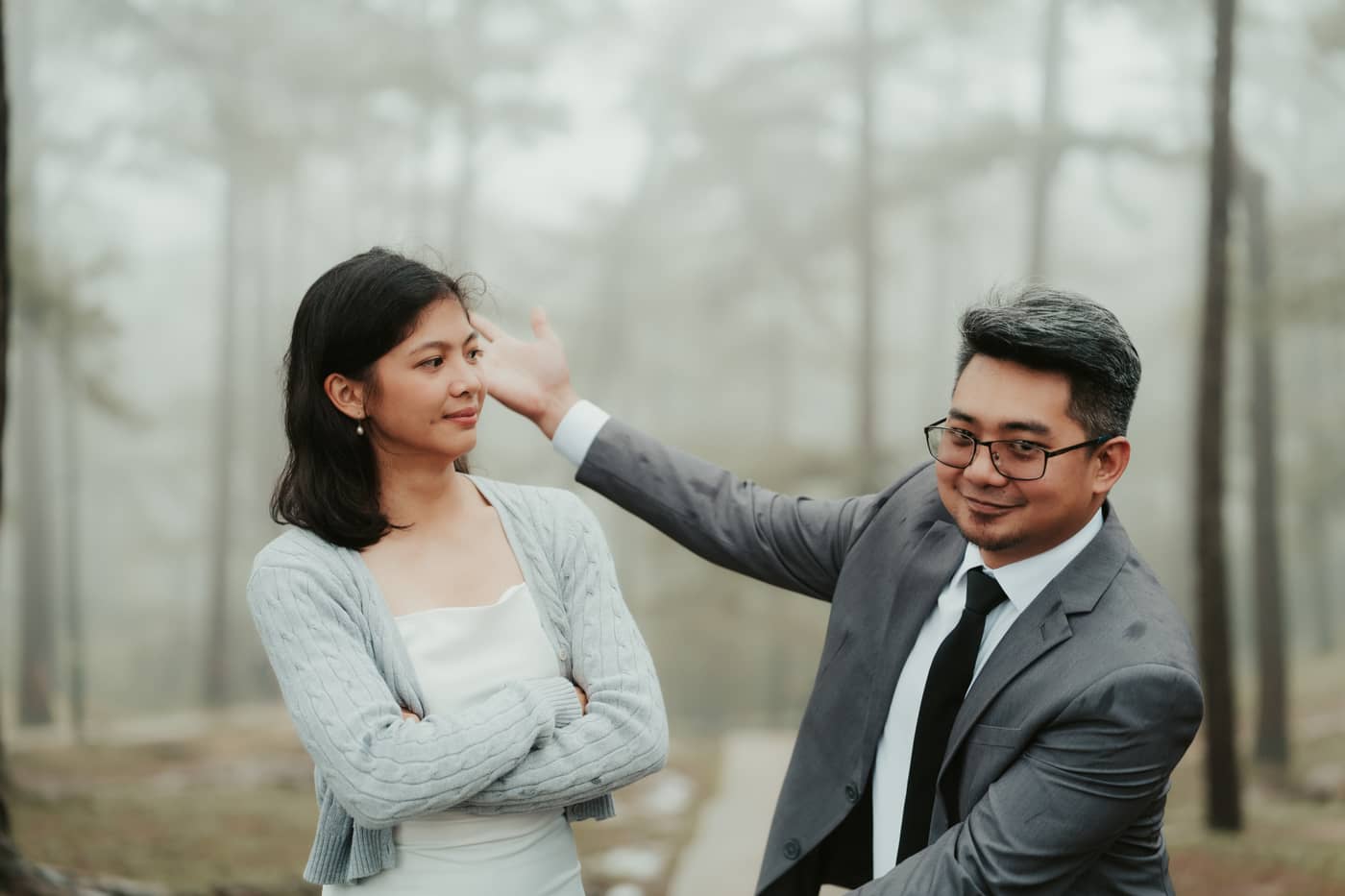 He playfully reaches toward her hair while she stands with her arms crossed