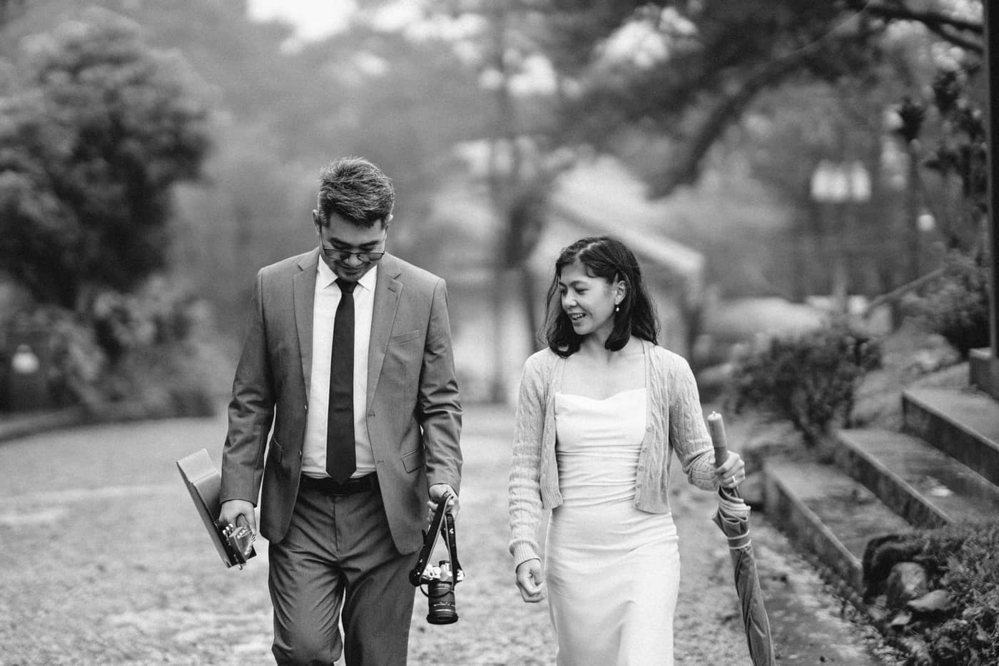 Black and white: the couple walking down a path with a camera and an umbrella
