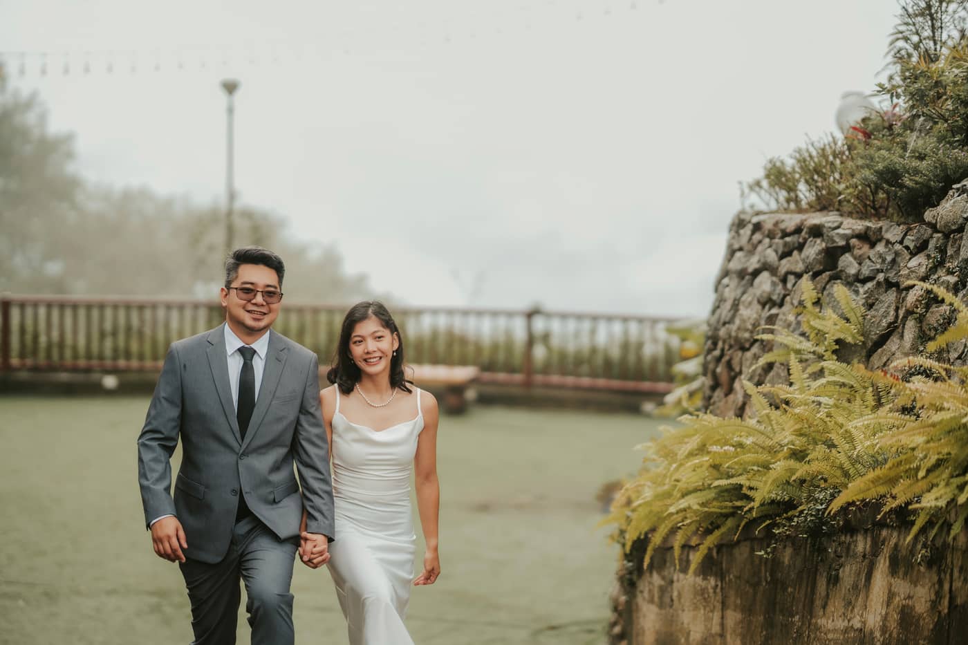The couple walking toward the camera beside a wall of ferns