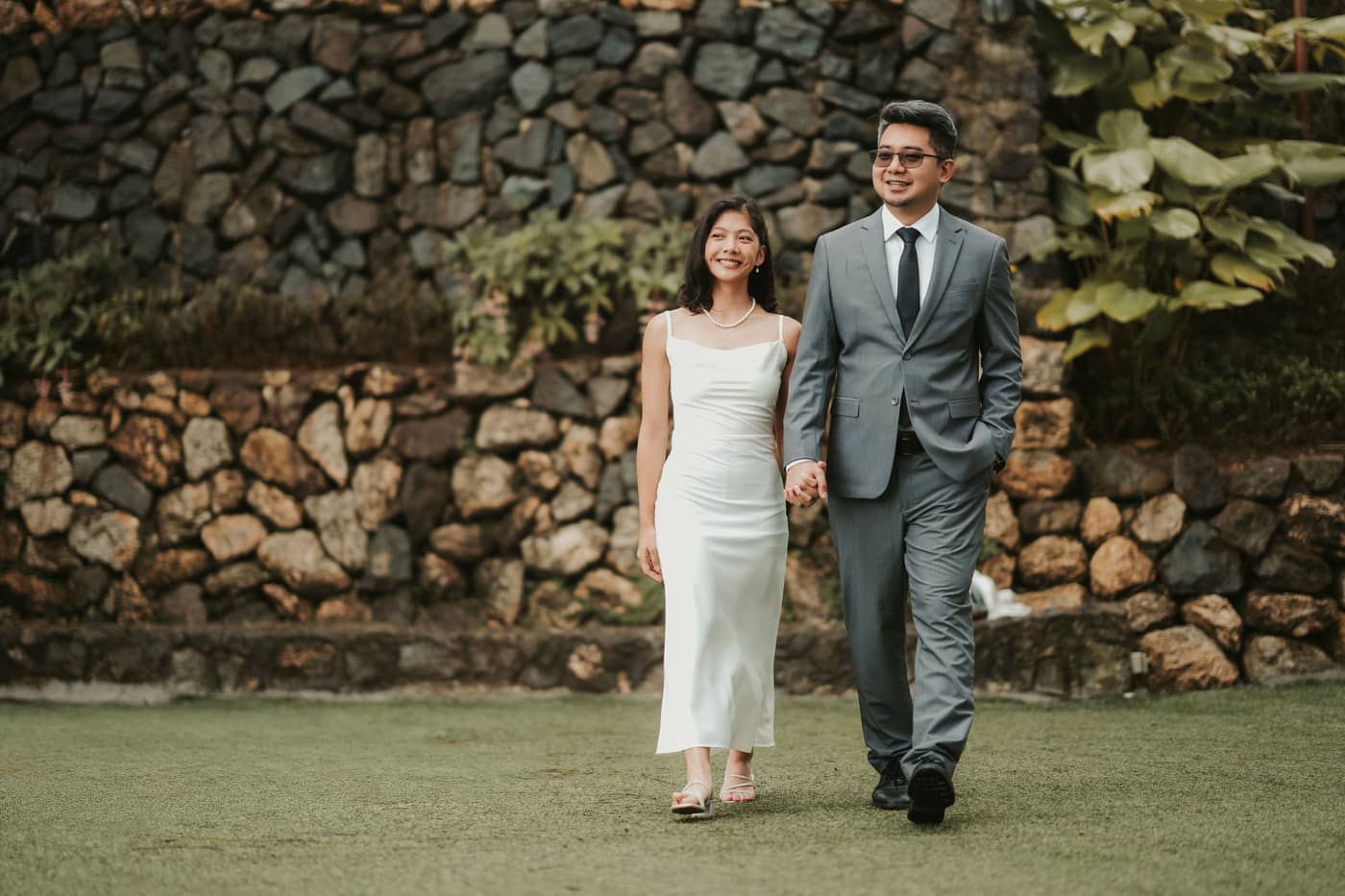 The couple walking hand in hand in front of a stone wall