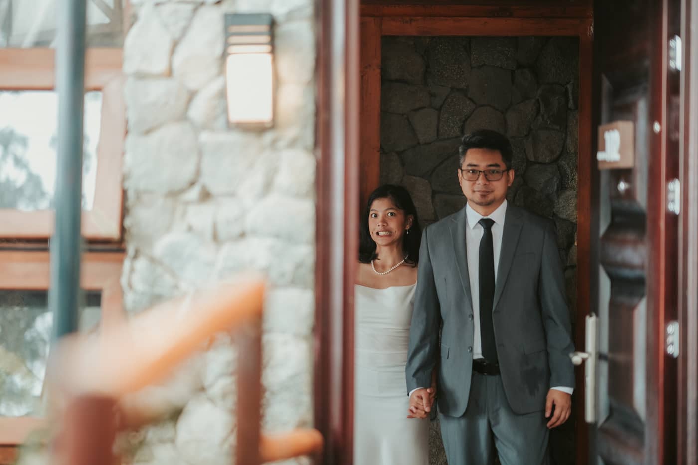 The couple peeking out from a doorway, her with a playful grin