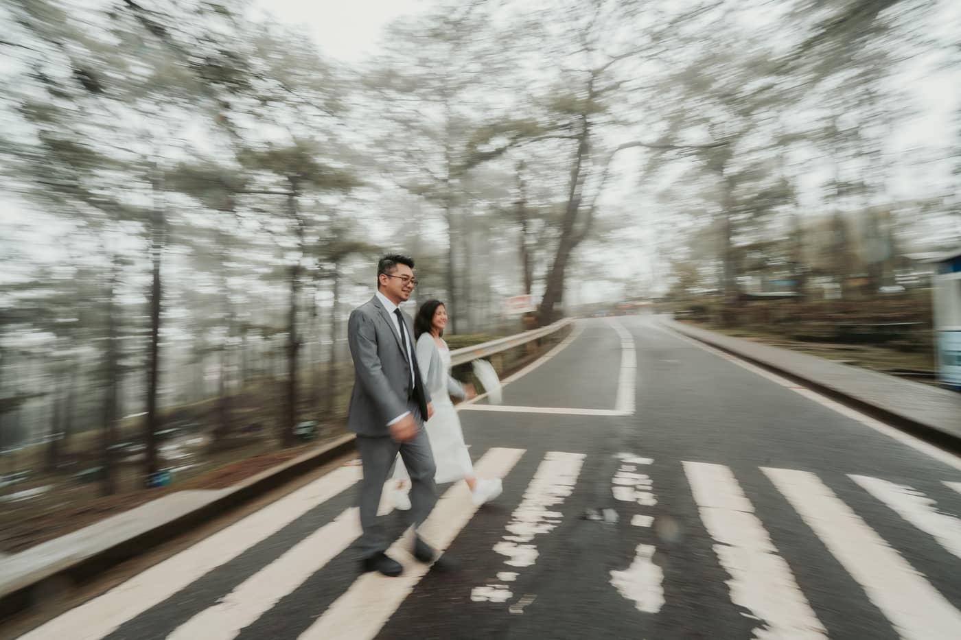 The couple walking across the road in a motion-blurred pine forest