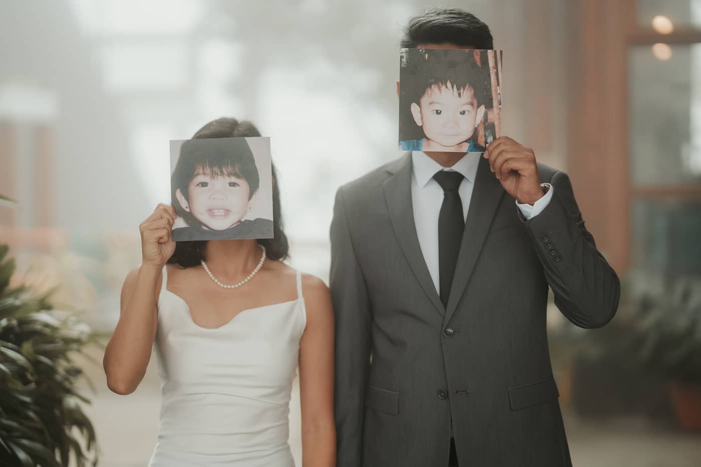 The couple each holding a childhood photo of themselves in front of their faces